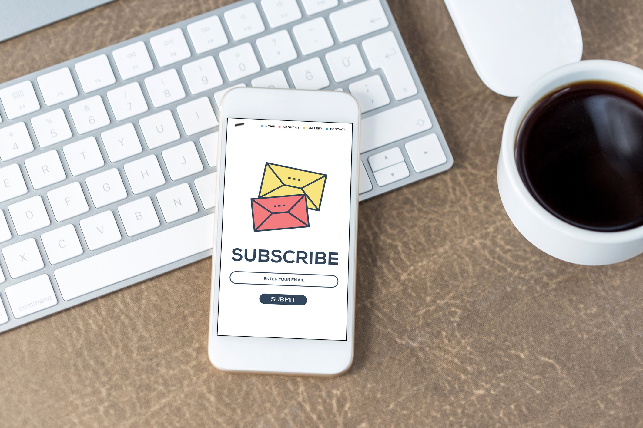 A mobile phone with a "Subscribe" screen, placed on a desk beside a keyboard and a cup of coffee.