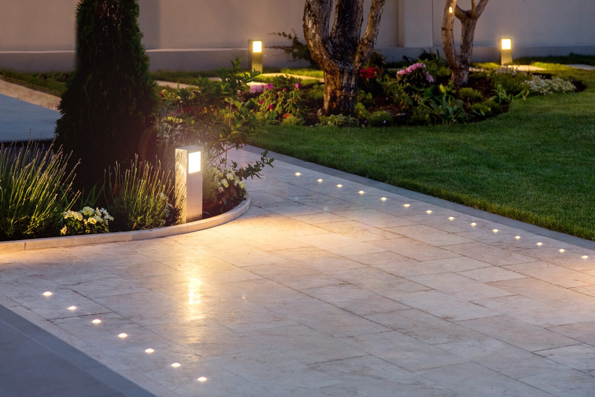 A beautifully lit garden pathway with surrounding foliage, decorative stone tiles, and small lanterns illuminating the evening landscape.