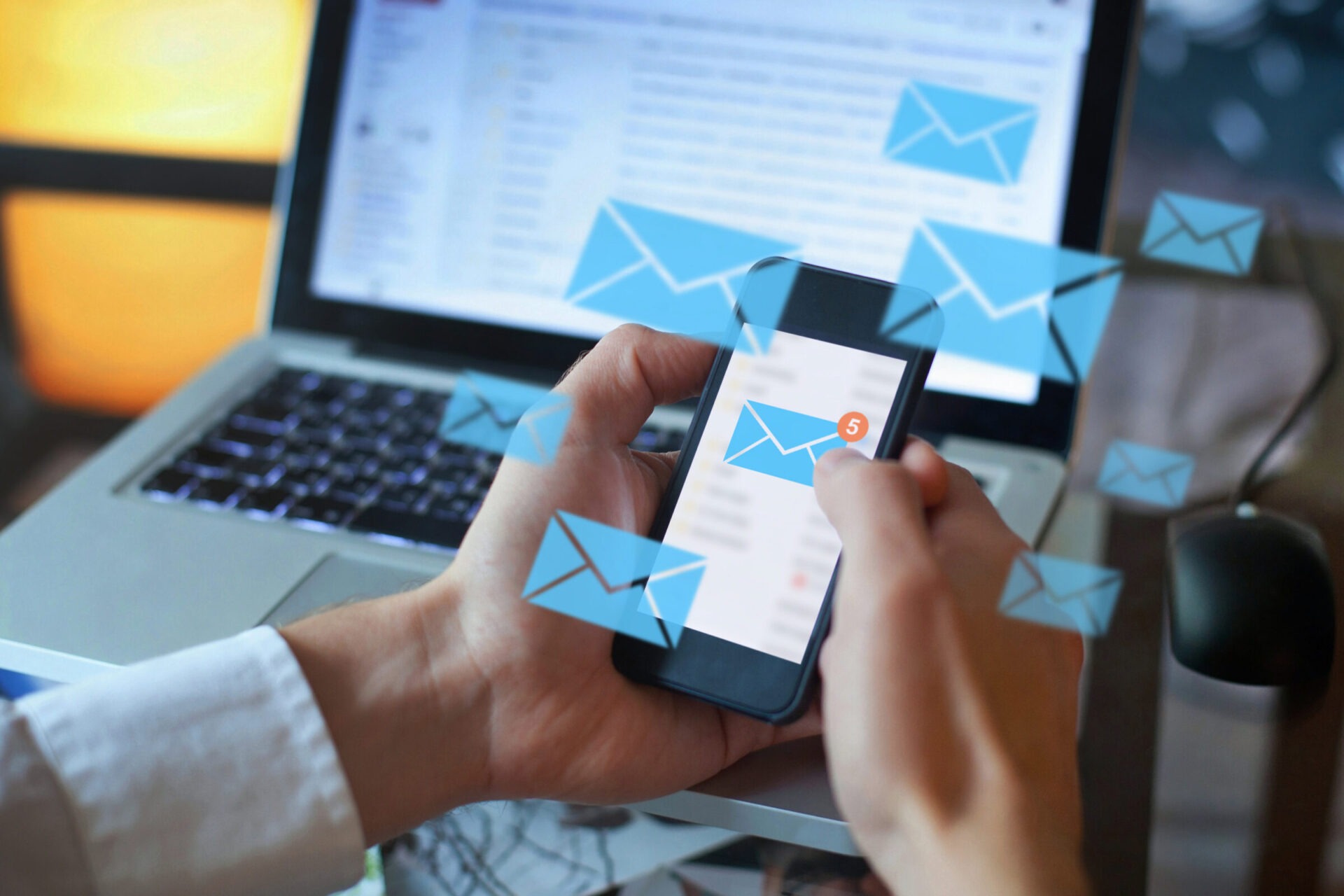 A person holds a smartphone displaying email notifications, with a laptop featuring an opened email application in the background. Animated envelopes are overlayed.