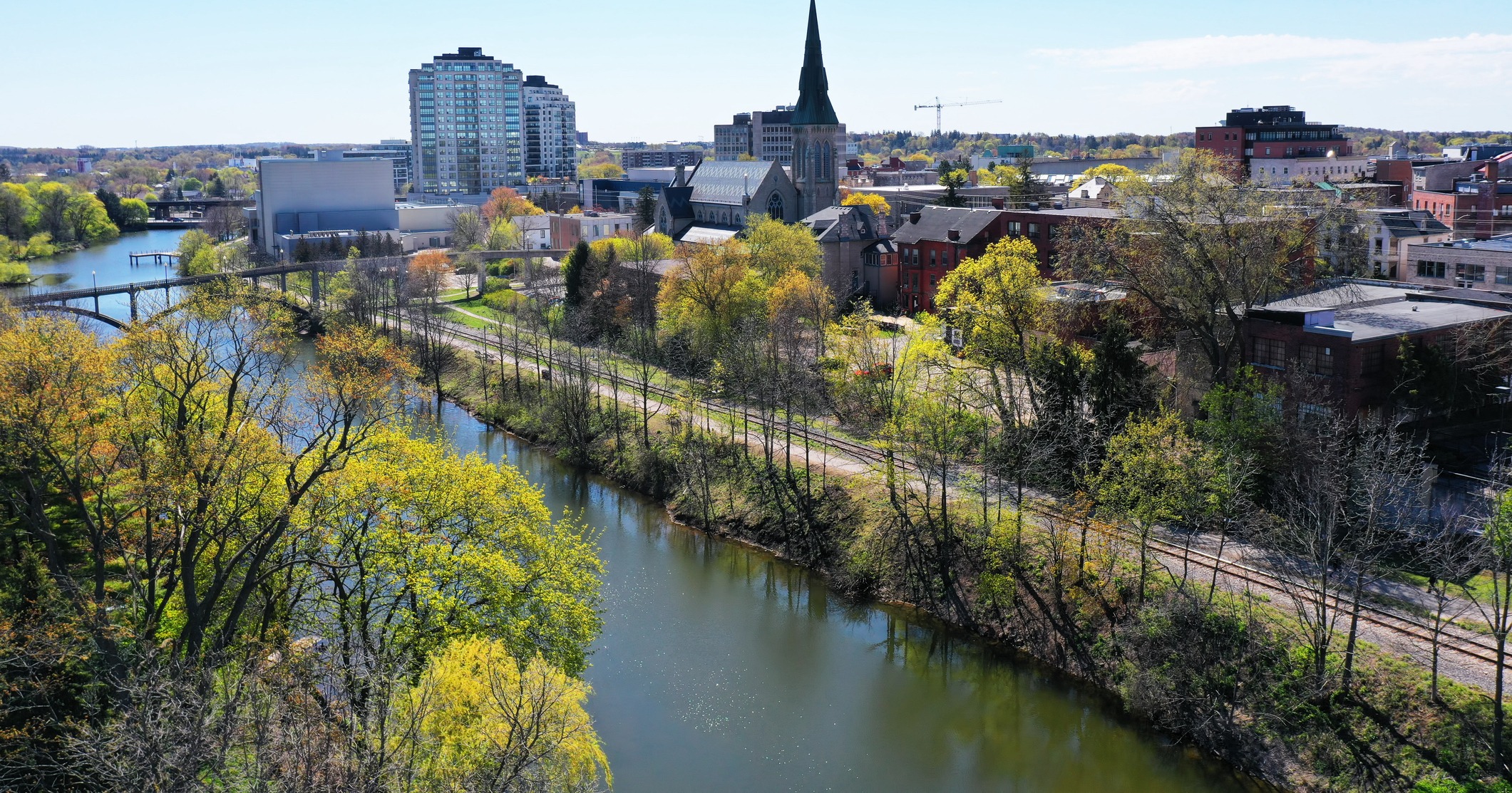 A scenic view of Perth featuring a serene river, lush greenery, the prominent St. John’s Church, and modern buildings in the background.