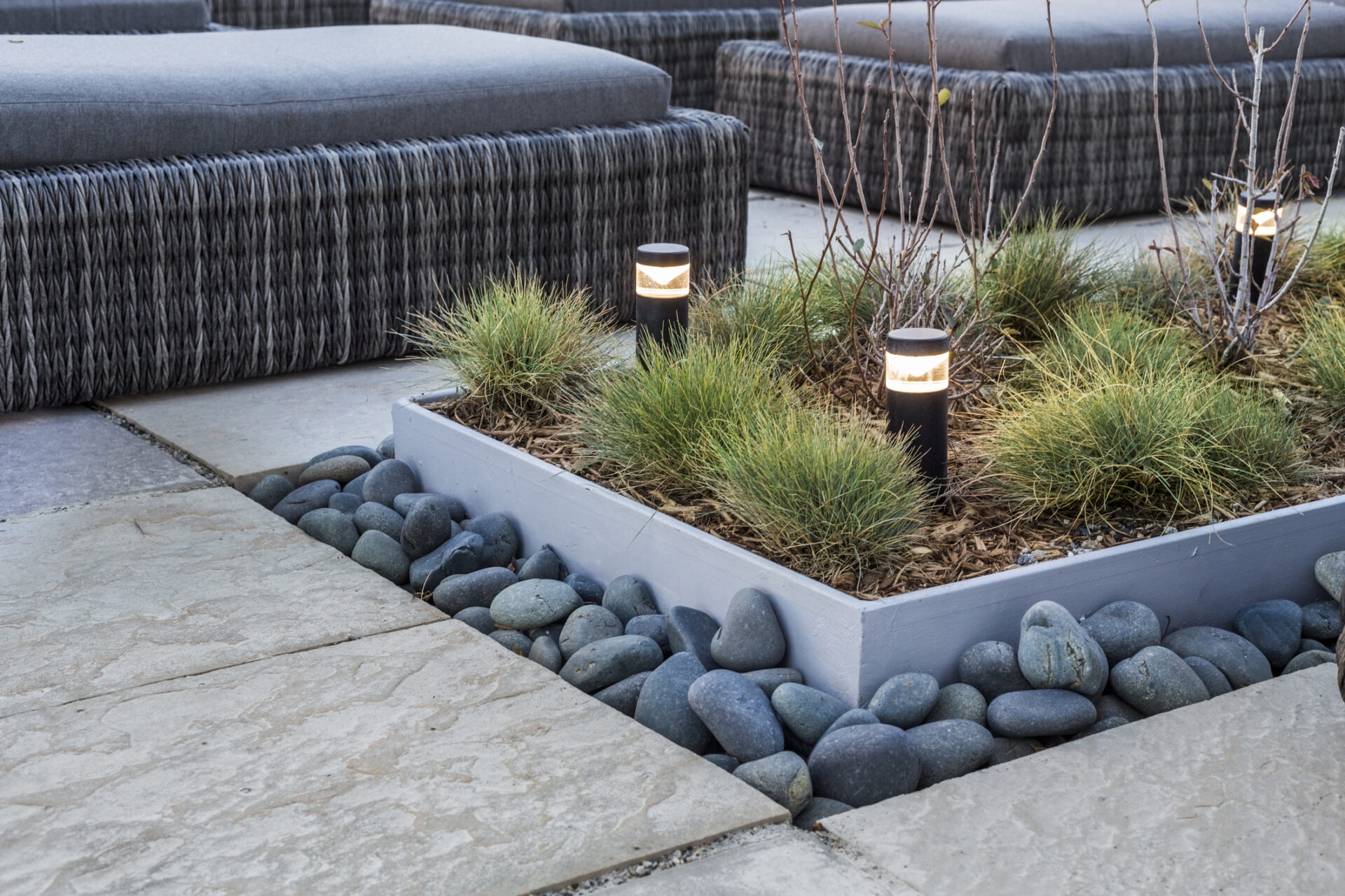 Modern outdoor seating area with wicker furniture, potted plants, decorative stones, and small pathway lights, creating a relaxing garden atmosphere.