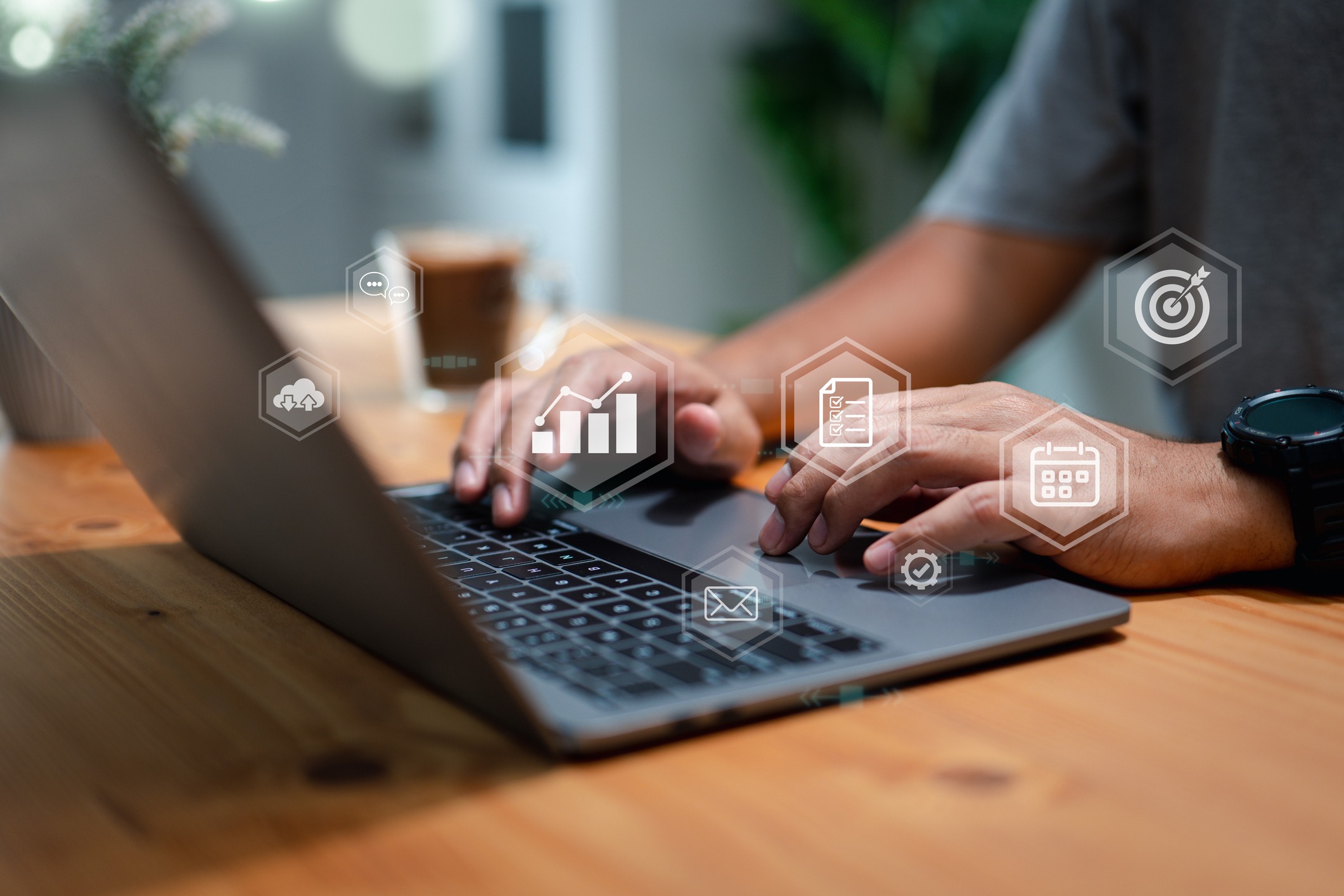 A person typing on a laptop at a wooden table, with various holographic icons representing business analytics, tasks, and communication.