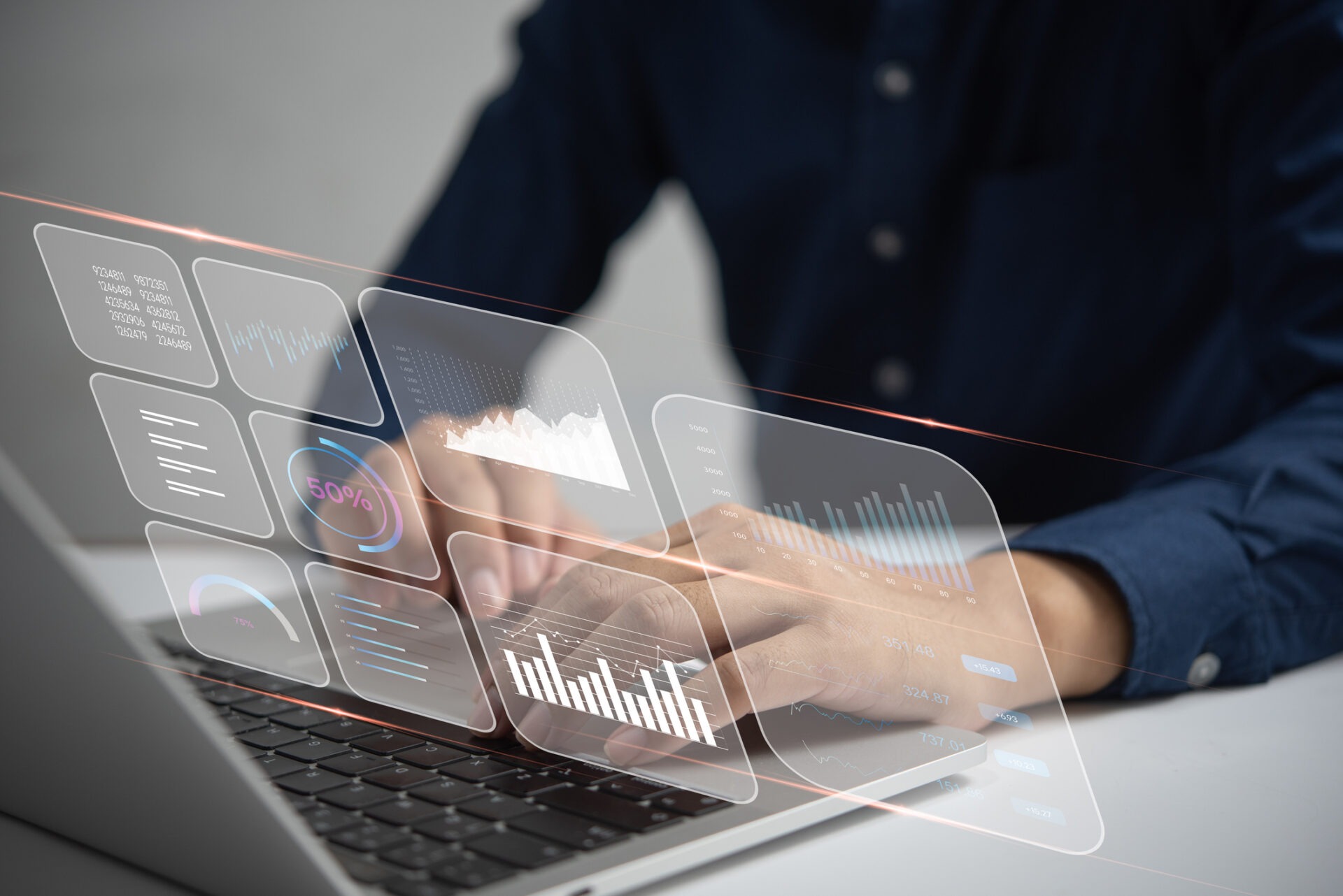 A person uses a laptop displaying transparent virtual charts and graphs, indicating data analysis or business visualization in a modern tech environment.