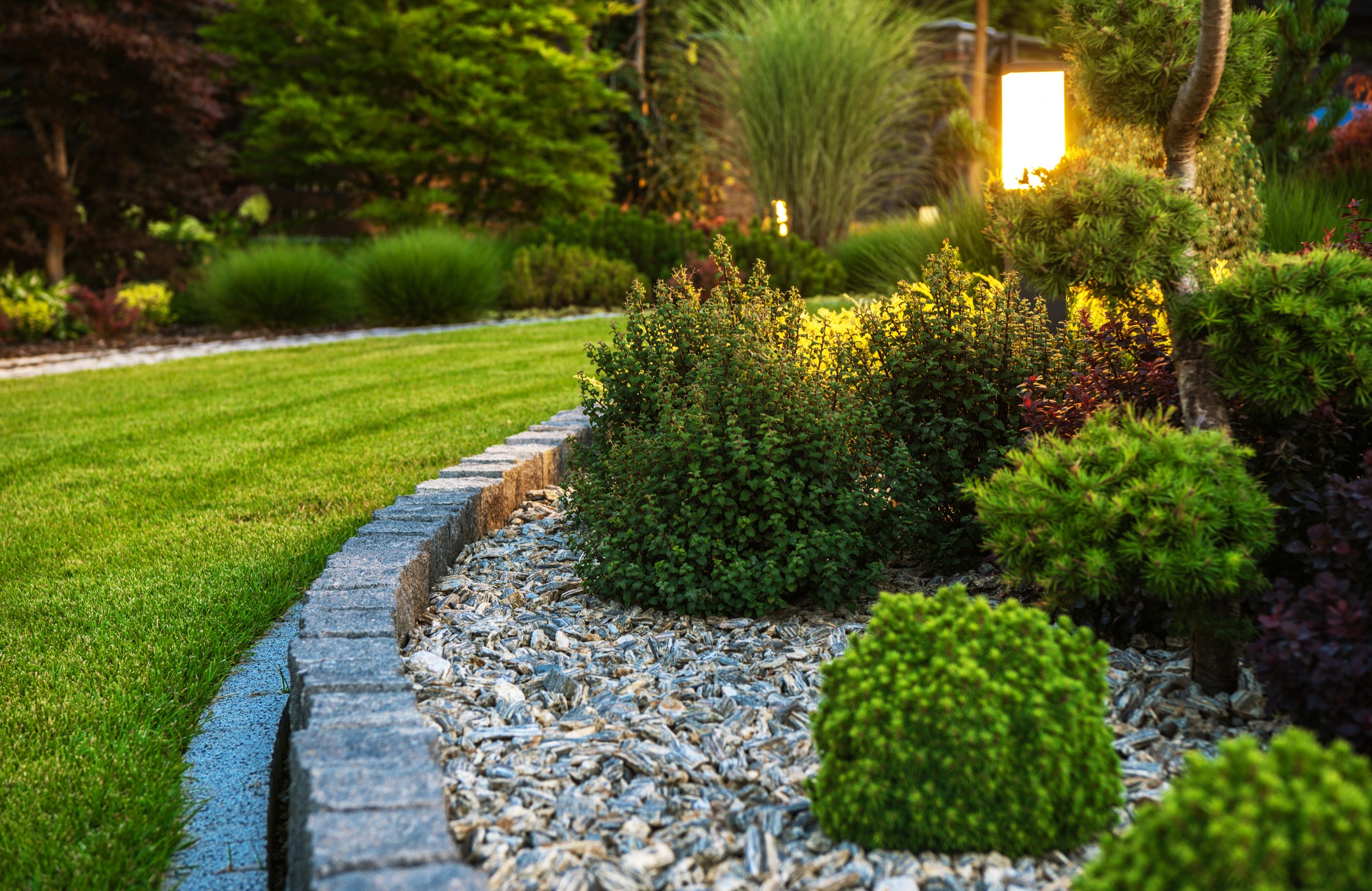 A well-manicured garden with lush greenery, a stone pathway, and ambient lighting, creating a serene and picturesque outdoor setting.