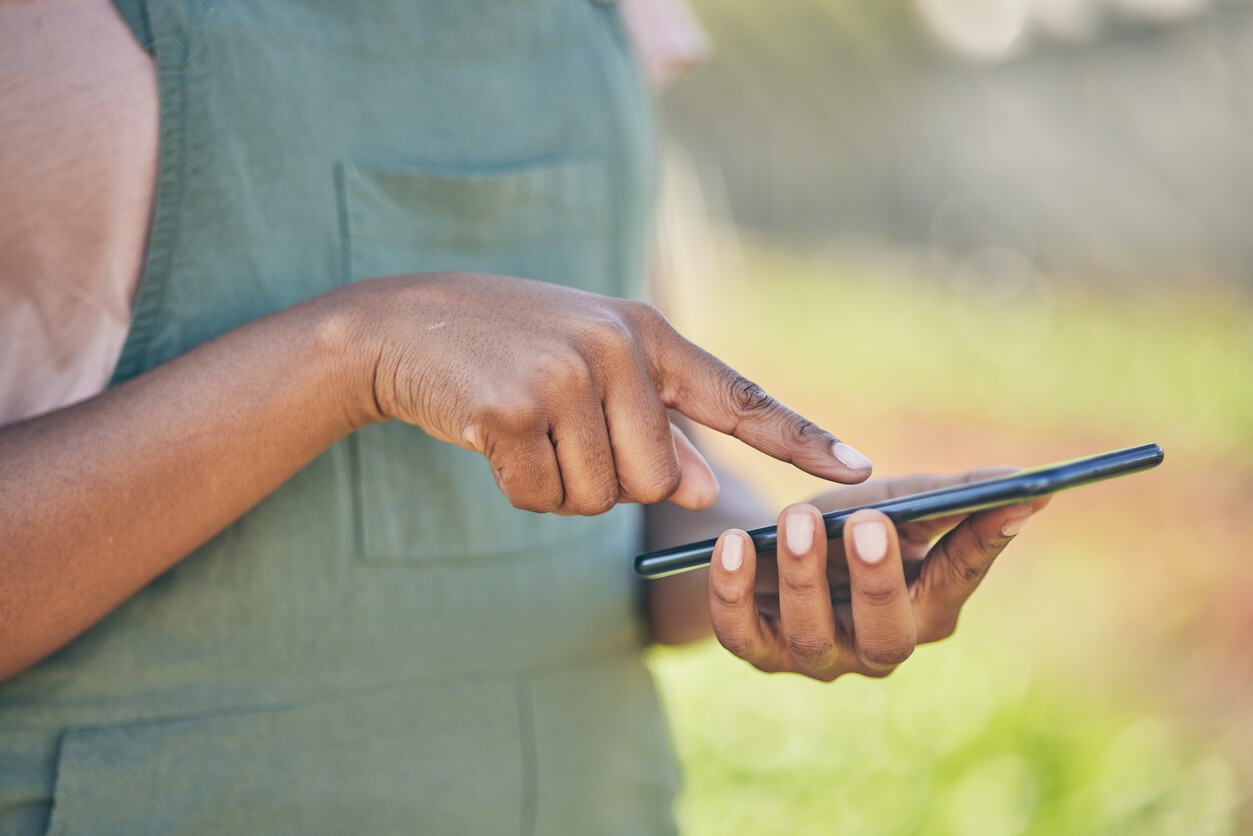 A close-up of a person using a smartphone outside, with a blurred green background and focusing on hands interacting with the device.