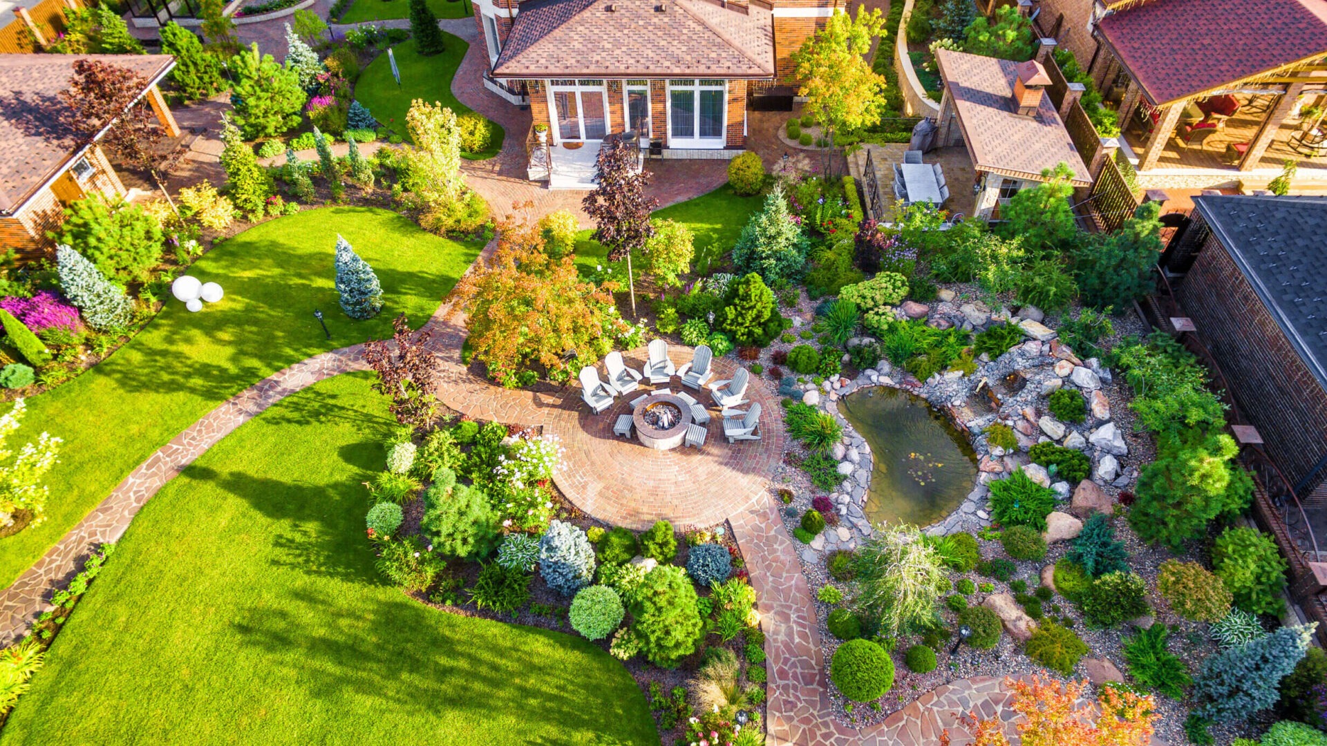 Landscape design with patio at residential house taken from above. Beautiful landscaping in home garden in summer. Aerial panoramic view of landscaped garden in backyard.