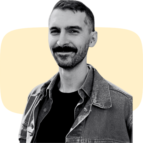 Man with a mustache smiling in black and white with yellow background